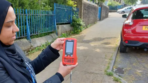 City of Bradford Metropolitan District Council Woman using an air quality monitor next to a school in Bradford