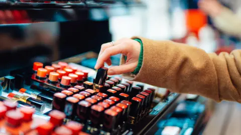 Getty Images Young women reaches for a lipstick at a make-up counter