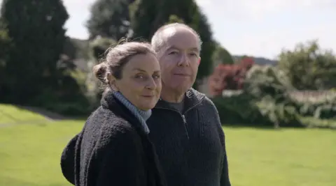 Andy Alcroft/BBC  Portrait of Fergus' parents standing in the park where the sapling will be planted.