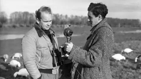 Peter Scott, the Director of the Severn Wild Fowl Trust, photographed at the headquarters of the Trust, Slimbridge, with Desmond Hawkins, BBC Features producer, West Region. Mr Hawkins is holding a microphone which has 