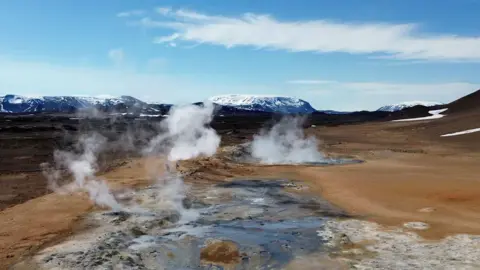 Steam rises from pools with snow-capped volcanos in the distance, in northeast in Iceland