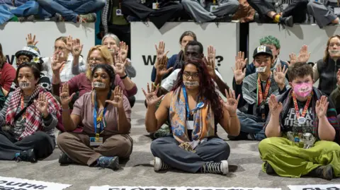 BBC Climate activists sitting on the floor wearing tape over their mouths, with 