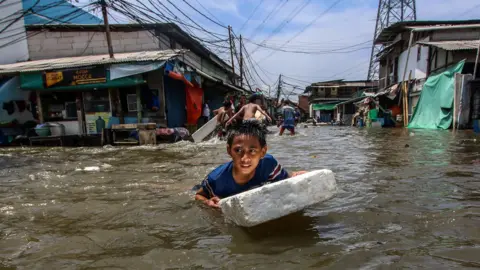 Eko Siswono Toyudho/Getty Images A boy struggling through a flooded street