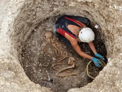 Bournemouth University A pit in a cemetary in Dorset showing a woman digging around skeleton bones