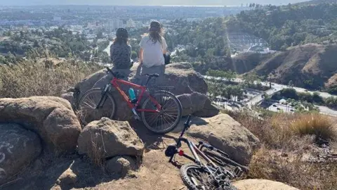 Two cyclists sit next to their bikes on a hill overlooking LA