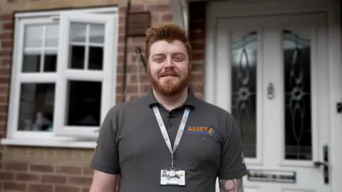 Kevin Church/BBC Tom Clarke is a white man with ginger hair and beard. He is wearing a grey T-shirt which reads