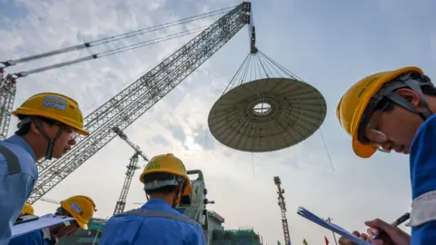 Getty Images Men with hard hats watch as a small dome from one of the world's first small modular nuclear reactor is lowered by giant cranes