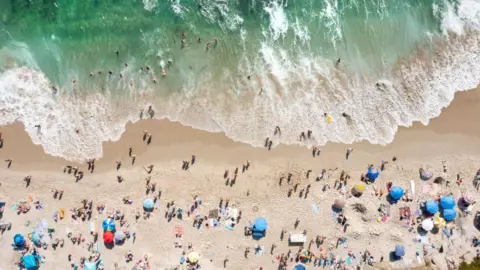Kevin Carter/Getty Images In an aerial view, people celebrate the Fourth of July along the coast of La Jolla's Windansea Beach on a warm summer day on July 4, 2023 in San Diego, California