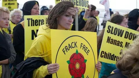 Getty Images A woman with brown hair and wearing a yellow jumper holds a yellow sign with the Lancashire rose in the centre and